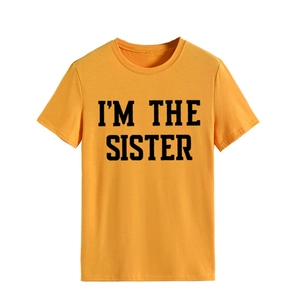 Gros plan sur le texte noir 'I'M THE SISTER' imprimé sur un T-shirt en coton jaune
