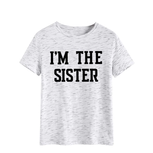 Gros plan du col rond gris chiné et de l'impression noire I'M THE SISTER sur le t-shirt