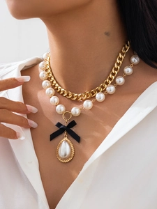Detail of layered gold curb chain and pearl necklace with a black ribbon bow and drop pearl