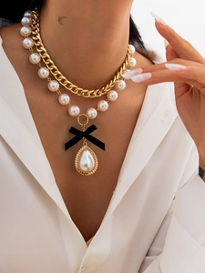 Close-up of double layer necklace with gold chain, black bow and drop pearl pendant