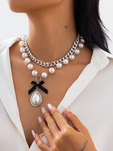 Detail of layered silver chain and pearl necklace with black bow and drop pearl pendant