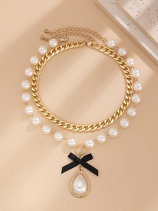 Detail of layered gold curb chain and pearl necklace with black bow and teardrop pendant