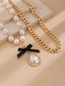 Detailed macro view of a black ribbon bow with a large teardrop pearl pendant on gold chain