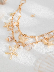 Detailed shot of layered gold body chain with starfish pendants and white pearls on sand