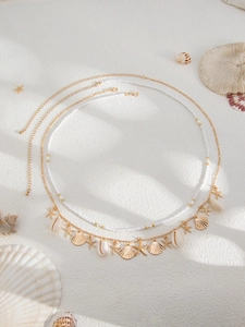 Detail of beach-style gold body chain with starfish pendants and white beads on sand