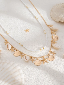 Detail of layered ocean necklace with gold starfish and shell charms on white texture
