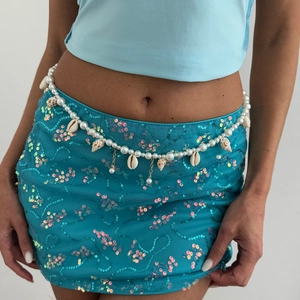 Detail of seashell pearl waist chain and sparkling blue sequin mini skirt for beach wear