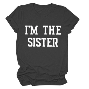 Gros plan du lettrage I'M THE SISTER blanc sur un t-shirt en coton gris foncé col rond