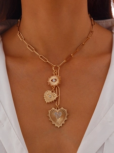 Detail of gold paperclip chain necklace with sun eye and textured heart pendants on a model