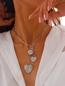 Detail of silver paperclip chain necklace with heart and eye charms on a model