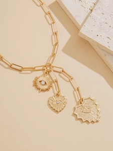 Macro shot of gold paperclip necklace with evil eye, heart, and sunburst charms