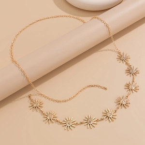 Détail d'une chaîne de taille dorée ornée de pendentifs soleil souriants sur fond chaud
