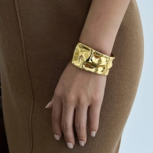 Close-up of a wide gold-tone irregular lava texture bracelet on a model's wrist