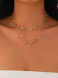 Close-up of a layered gold necklace with bezel-set crystals on a model wearing white
