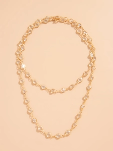 Detail of double-layer gold necklace featuring faceted crystal accents on a pink surface