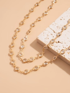 Detail of gold Y-necklace featuring bezel-set round crystals on a textured stone surface