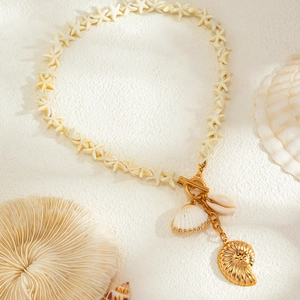 Detail of seashell necklace with starfish beads and golden nautilus charm on beach sand