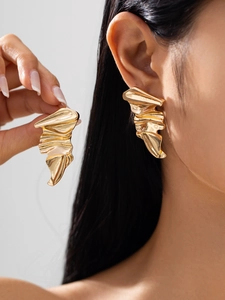 Close-up of abstract large gold earrings with irregular folded texture on a female model