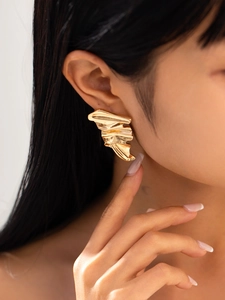 Close-up of model wearing gold irregular pleated earrings with a folded fan-like metal design