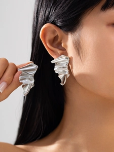 Macro detail of irregular wrinkled silver stud earrings on a model with metallic texture