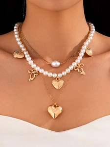 Detail of layered gold-tone necklace with pearls and heart pendants on a model