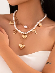 Detail of layered gold-tone necklace with white faux pearls and heart shaped pendants
