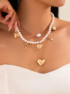 Detail view of multi-layered gold heart necklace with pearls and elegant bow charms