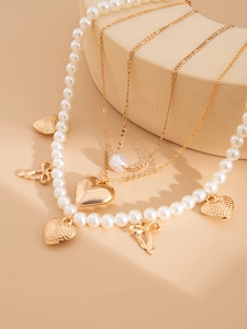 Close-up of layered pearl and gold heart necklace with bow pendant on a beige display