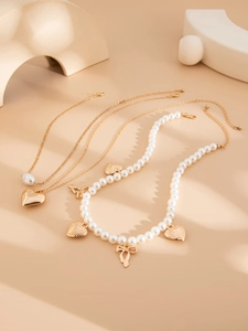 Detail of layered gold necklaces with faux pearls, hollow hearts and ribbon bow pendants