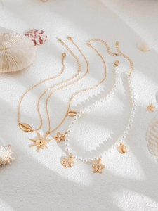 Detail view of ocean-themed necklaces with pearls, starfish, and shells on white sand