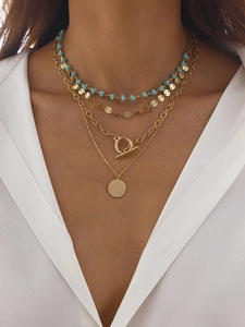 Détail du collier multicouche doré avec perles bleues, fermoir OT et pendentif