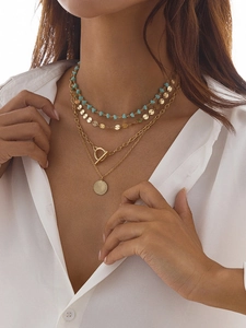 Détail de colliers dorés superposés avec perles turquoise et pendentif pièce sur un mannequin