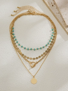 Vue détaillée du collier multi-rangs doré avec pendentif pièce, perles turquoise et fermoir OT