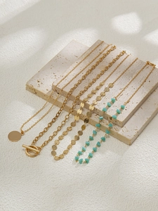 Détail de colliers dorés superposés avec pendentif pièce, fermoir OT et perles turquoise