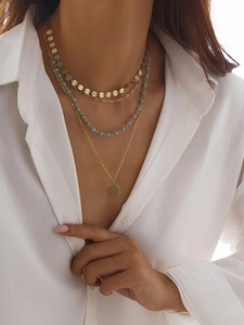 Détail d'un collier bohème doré à quatre rangs avec pendentif pièce et perles bleues sur modèle