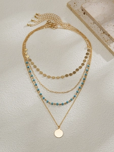 Détail d'un collier doré multicouche avec perles bleues et pendentif sur pierre