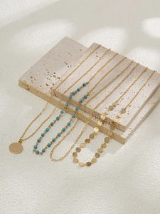 Détail de colliers dorés superposés avec perles turquoises et pendentifs de pièces