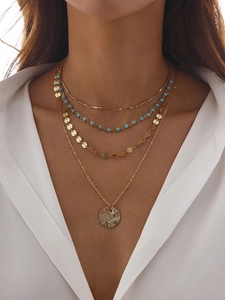Détail de colliers dorés superposés avec perles bleues, sequins et pendentif médaille