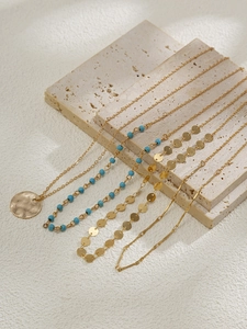 Détail de colliers superposés dorés avec pendentif pièce et chaîne de perles turquoise