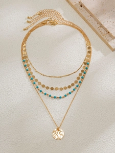 Détail du collier multicouche doré avec perles turquoise et pendentif disque martelé