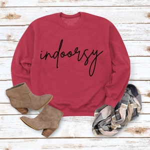 Flat lay of brick red sweatshirt with indoorsy print and plaid scarf on wood floor