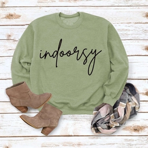 Detailed flat lay of green crewneck sweatshirt with 'indoorsy' print on white wood