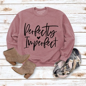 Flat lay of pink sweatshirt with Perfectly Imperfect lettering and heart on wooden background