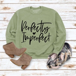 Flat lay of sage green sweatshirt with Perfectly Imperfect print and plaid scarf