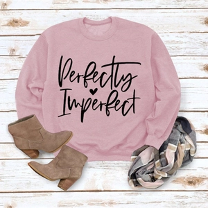 Flat lay of pink sweatshirt with Perfectly Imperfect lettering on white wood floor