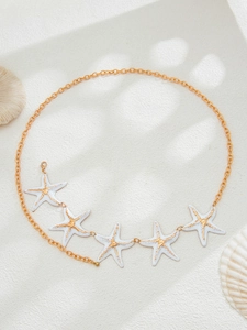 Detail of golden starfish waist chain with enamel charms on beach themed background