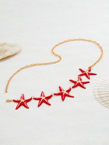 Detail of gold waist chain with five red starfish charms on a white sandy beach background