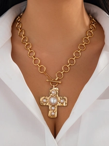 Detail of gold cross pendant with pearls on chunky chain worn by a model in white shirt