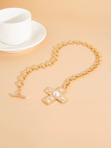 Close-up of gold chain necklace featuring a cross pendant with pearl inlays and OT buckle