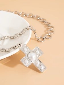 Close-up of silver cross pendant with inlaid pearls on a textured metal chain